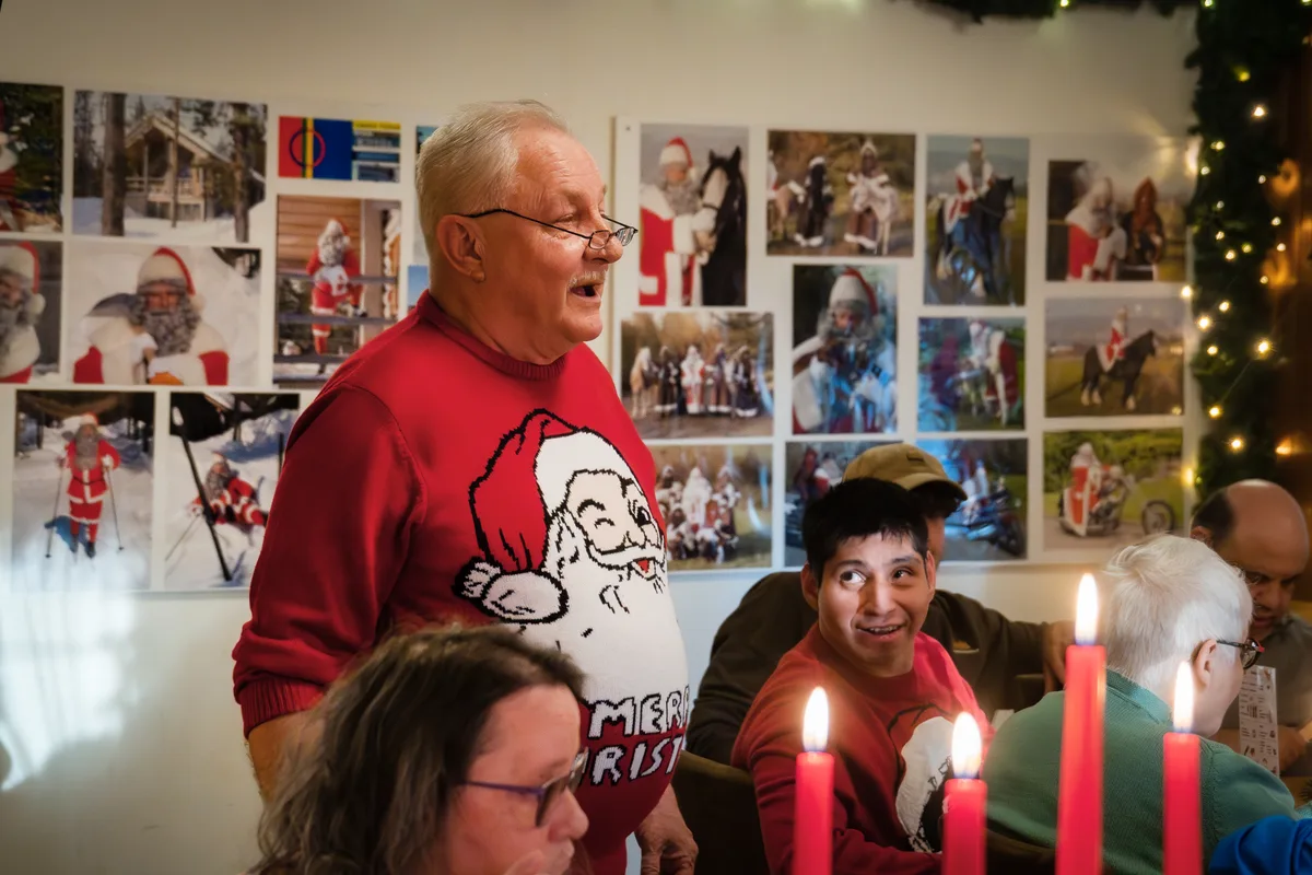 Ein Mann mit einem Weihnachtspulli trägt ein Versli den Gästen vor.